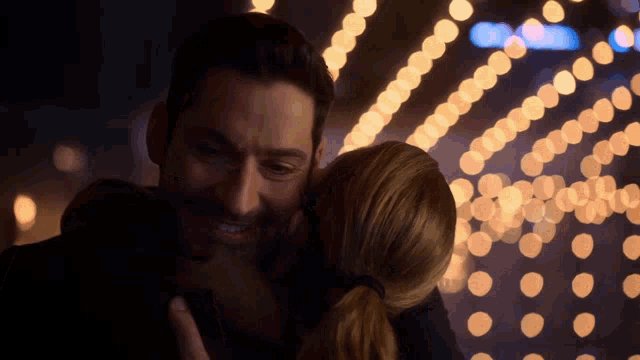 a man and a woman are hugging in front of a blurry background of lights