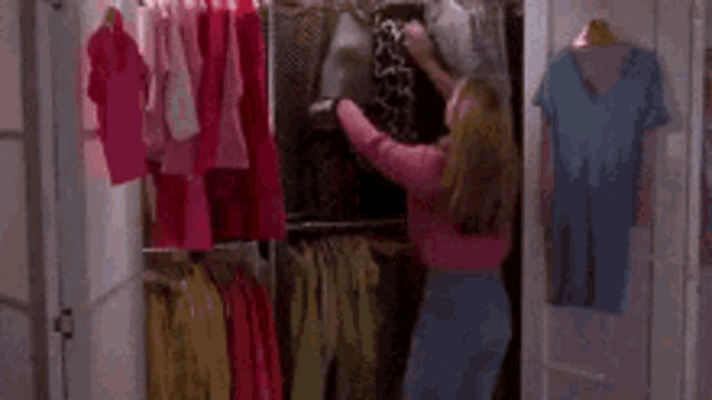 a woman in a pink shirt is standing in front of a rack of clothes .