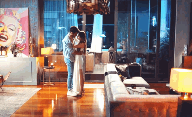 a man and woman are hugging in a living room with a marilyn monroe painting on the wall