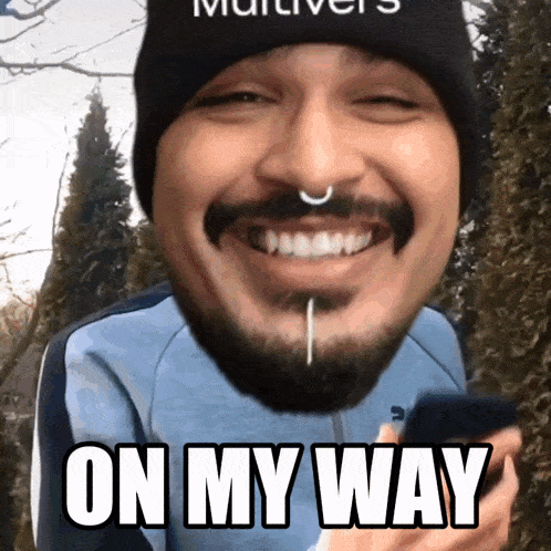 a man with a beard and a nose ring is smiling and holding a cell phone with the words on my way above his head