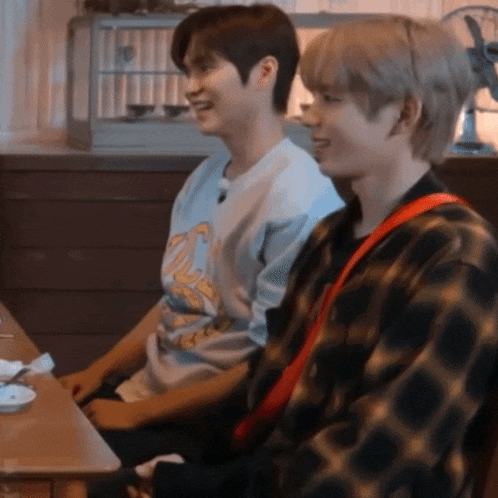 two young men are sitting at a table smiling .