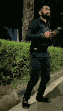 a man with a beard is walking down a street while looking at his phone