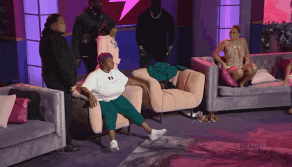 a woman is sitting on a couch with her legs crossed while a group of people watch .