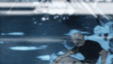 a man in a black shirt is sitting in a pool of water with the word nsnlxd on the bottom right
