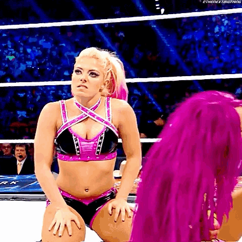 a woman in a pink and black outfit is kneeling down in a wrestling ring with another woman .