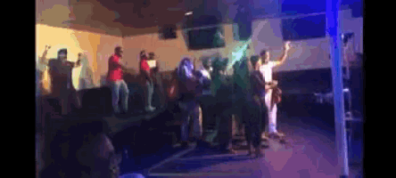 a group of people are dancing in a dark room with purple lights .