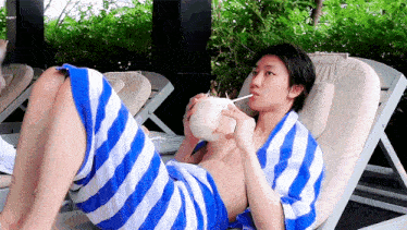 a shirtless man is wrapped in a blue and white striped towel and drinking from a coconut