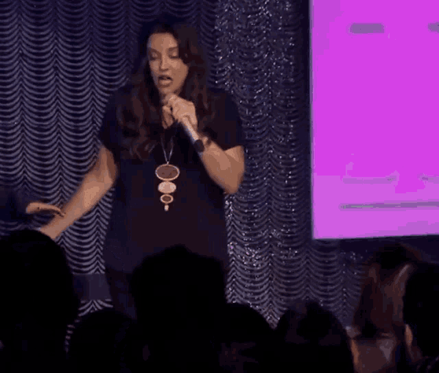 a woman sings into a microphone in front of a purple screen
