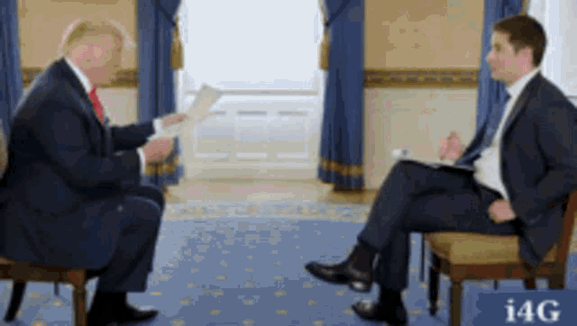 a man in a suit and tie is sitting next to another man