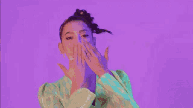a woman is making a peace sign with her hands while wearing a blue and green jacket .