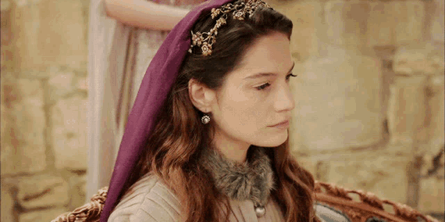 a woman wearing a purple head scarf and earrings is sitting in a chair