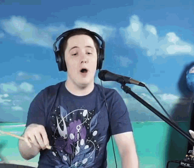 a man wearing headphones is singing into a microphone while holding a drum stick .
