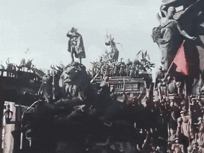 a crowd of people are gathered around a statue of a woman holding a red flag