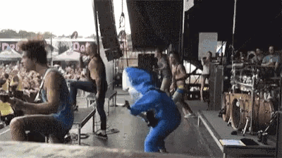 a man in a blue shark costume is playing a guitar on stage