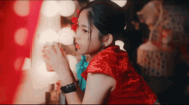 a woman in a red dress with a flower in her hair looks at herself in a mirror