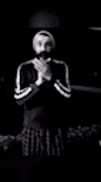 a man wearing a mask is standing in the dark with his hands folded in prayer .