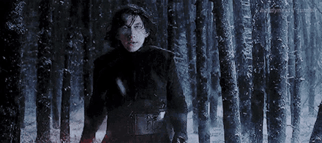 kylo ren is standing in a snowy forest holding a lightsaber .