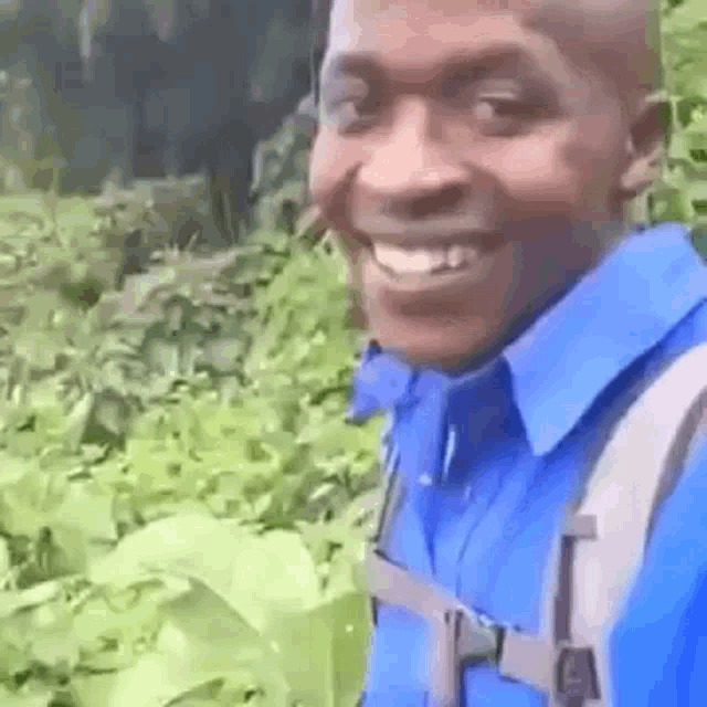 a man wearing a blue shirt and a backpack is smiling while standing in the woods .