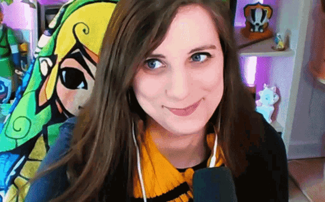 a woman wearing headphones and a scarf smiles in front of a cartoon character
