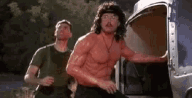 a man without a shirt is standing next to another man in front of a truck .