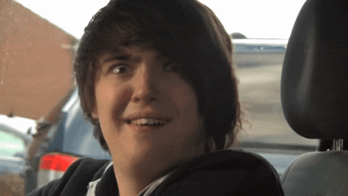 a young boy with dark hair is smiling in a car seat