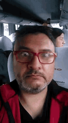 a man with glasses and a beard is sitting in a bus with apolo written on the back seat