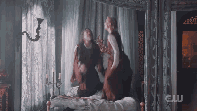 a man and a woman are sitting on a bed with a cw logo on the bottom right