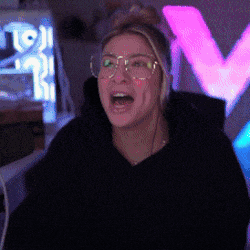 a woman wearing glasses and a black hoodie is screaming in front of a neon sign that says v