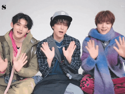 three young men are sitting next to each other with their hands in the air and the letter s is on the bottom right