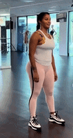 a woman is standing in a gym wearing a white tank top and pink leggings .
