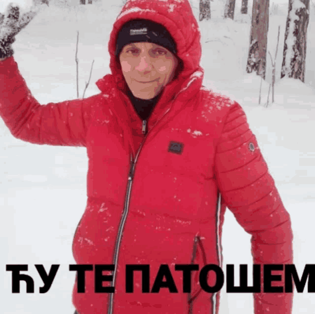 a man wearing a red jacket and a black hat is standing in the snow with the words " by te patohem " below him