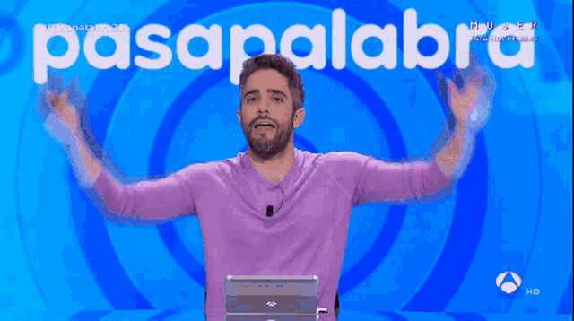 a man in a purple sweater is standing in front of a sign that says pasapalabra
