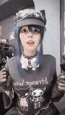a girl with blue hair is wearing a hat and a sweater with a cat on it .
