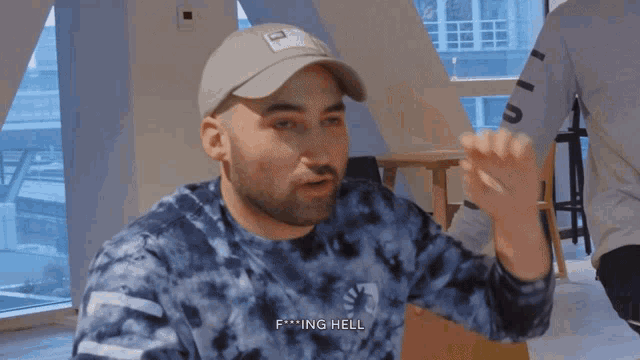a man wearing a tie dye shirt and a hat says f * ing hell