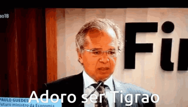 a man in a suit and tie is speaking into a microphone with the words adoro ser tigrao behind him