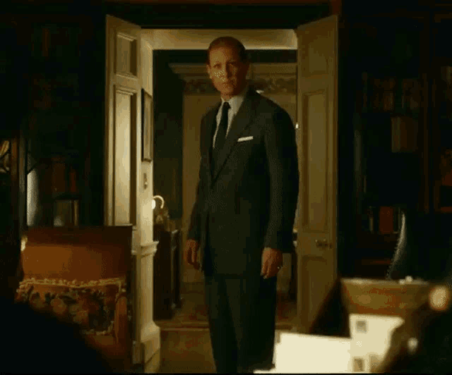 a man in a suit and tie is standing in a living room with his door open .