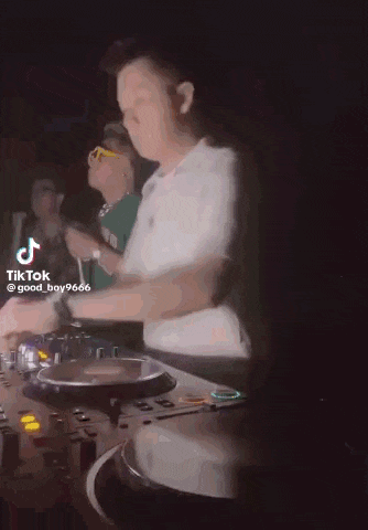 a man in a white shirt is playing music on a turntable in a club .
