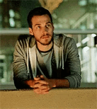 a man with a beard is leaning against a wall with his hands folded and looking up .