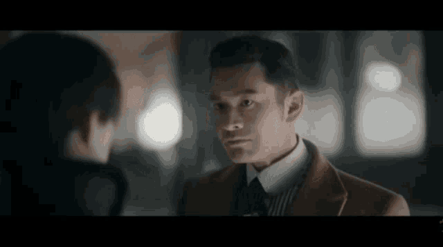a man in a suit and tie is standing next to another man in a dark room .