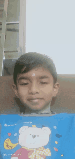 a boy wearing a blue shirt with a teddy bear on it is sitting on a couch
