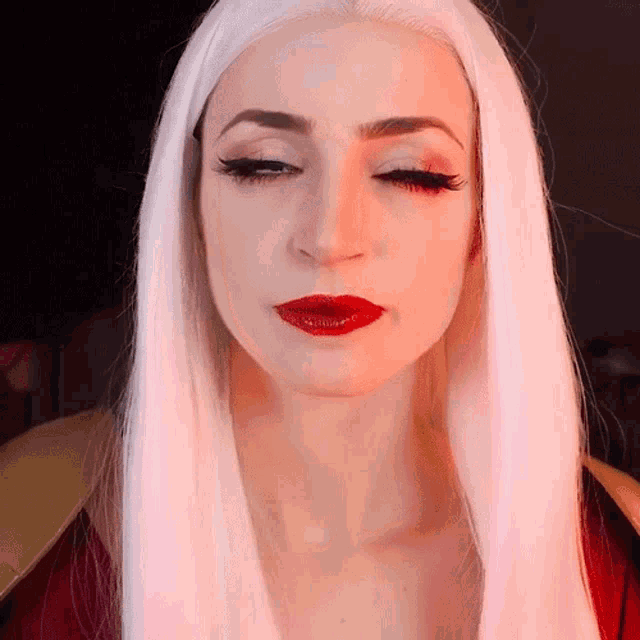 a woman with white hair and red lipstick looks down