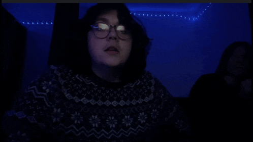 a person with glasses sticking their tongue out in a dark room