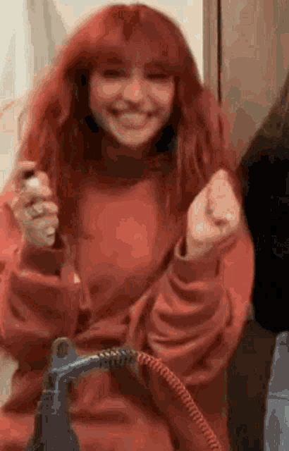 a woman with red hair is smiling while holding a hair dryer and blow drying her hair .