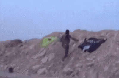 a man is holding a green flag in the air while standing on top of a sandy hill .