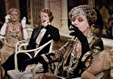 a woman in a tuxedo is drinking from a glass while sitting next to two other women