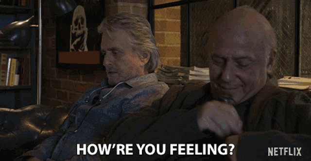 two men are sitting on a couch and one of them is asking the other how he 's feeling