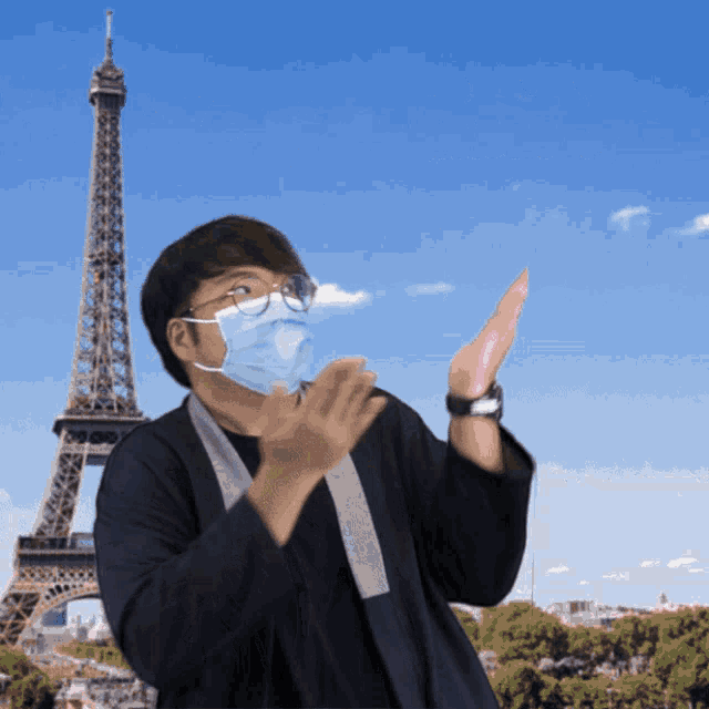 a man wearing a face mask and glasses is clapping in front of the eiffel tower