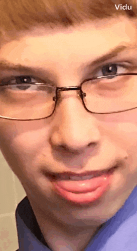 a young man wearing glasses and a blue shirt has his tongue hanging out