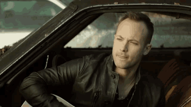 a man in a black leather jacket is sitting in a car holding a guitar