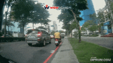 a car is driving down a street next to a scooter and a sign that says wow tchout